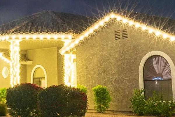 Warm white C9 roofline lights outlining a covered entry, gable and arched windows on a stucco home
