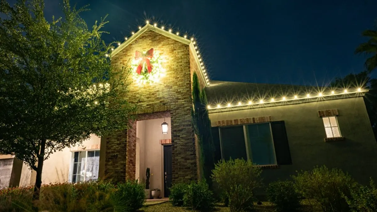 Lit wreath with a red bow on a stone gable above the front door, warm white C9 lights along the roofline